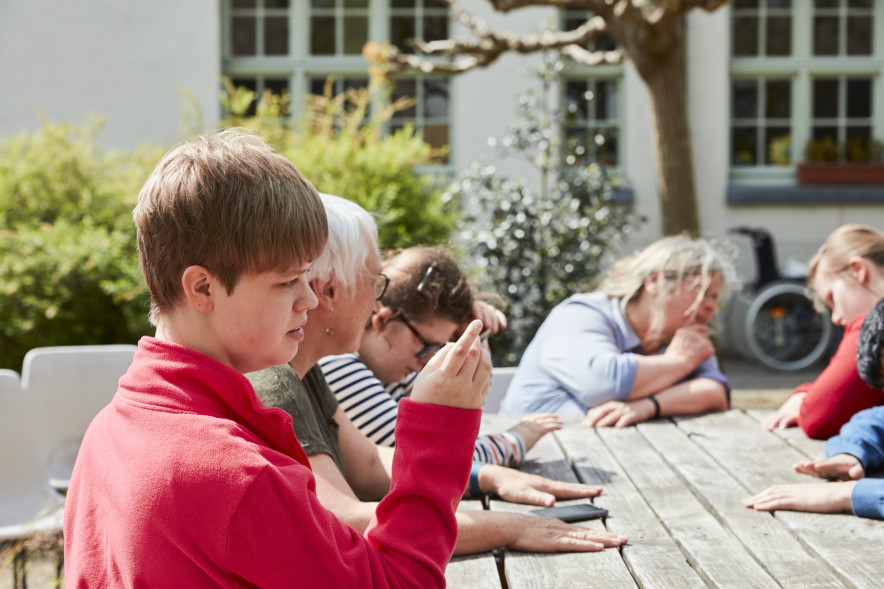 Tieners met beperking zitten rond houten tuintafel met begeleidsters
